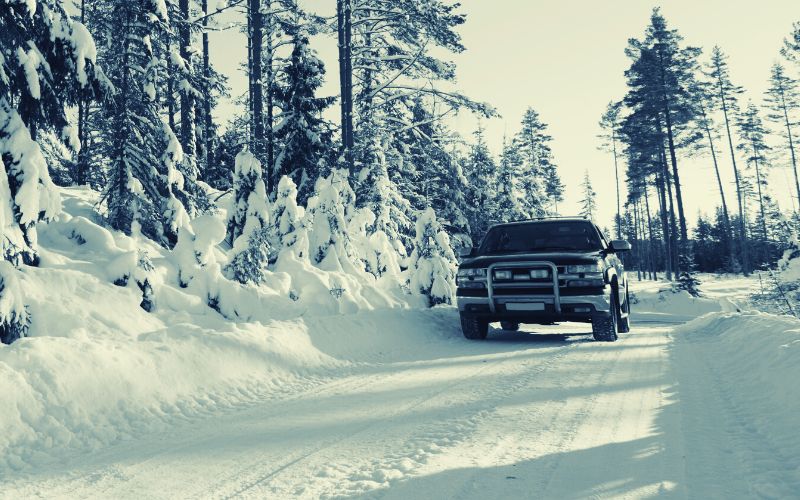 black pickup truck driving on a snowy road surrounded by snow-covered trees